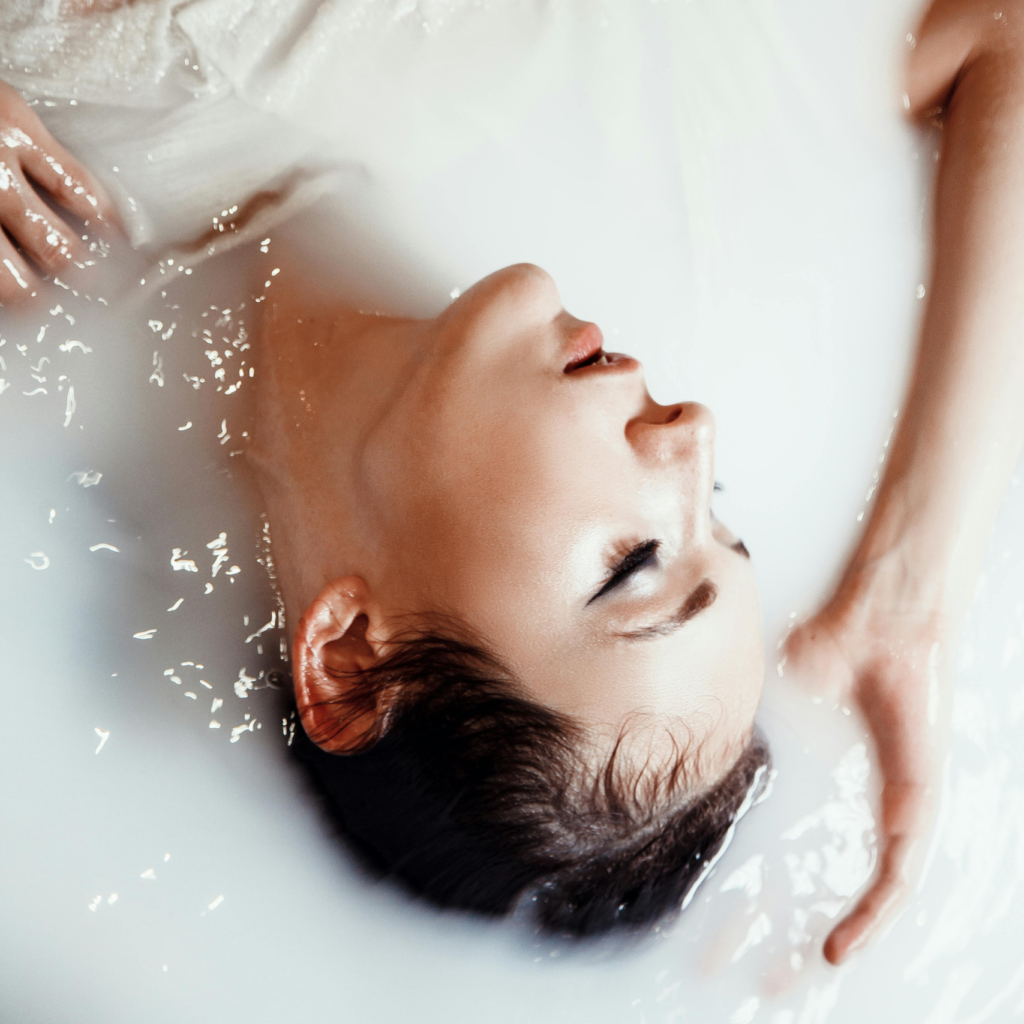 A serene woman resting in a milky white bath with soft lighting, creating a calm and feminine spa-like atmosphere.